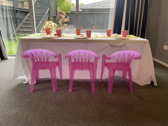 A Playday trestle table covered with a white tablecloth, with three pink children’s chairs in front.