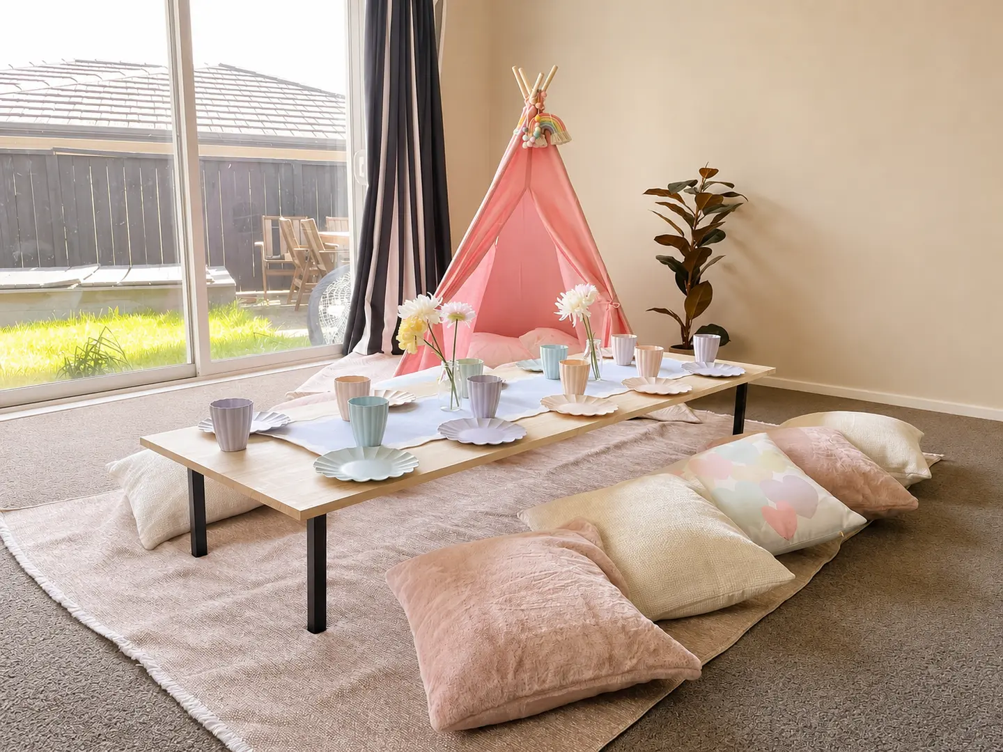 A real Playday picnic setup for children with a low wooden table, pastel flower-shaped plates and cups, soft floor cushions, flower vases and a pink teepee.