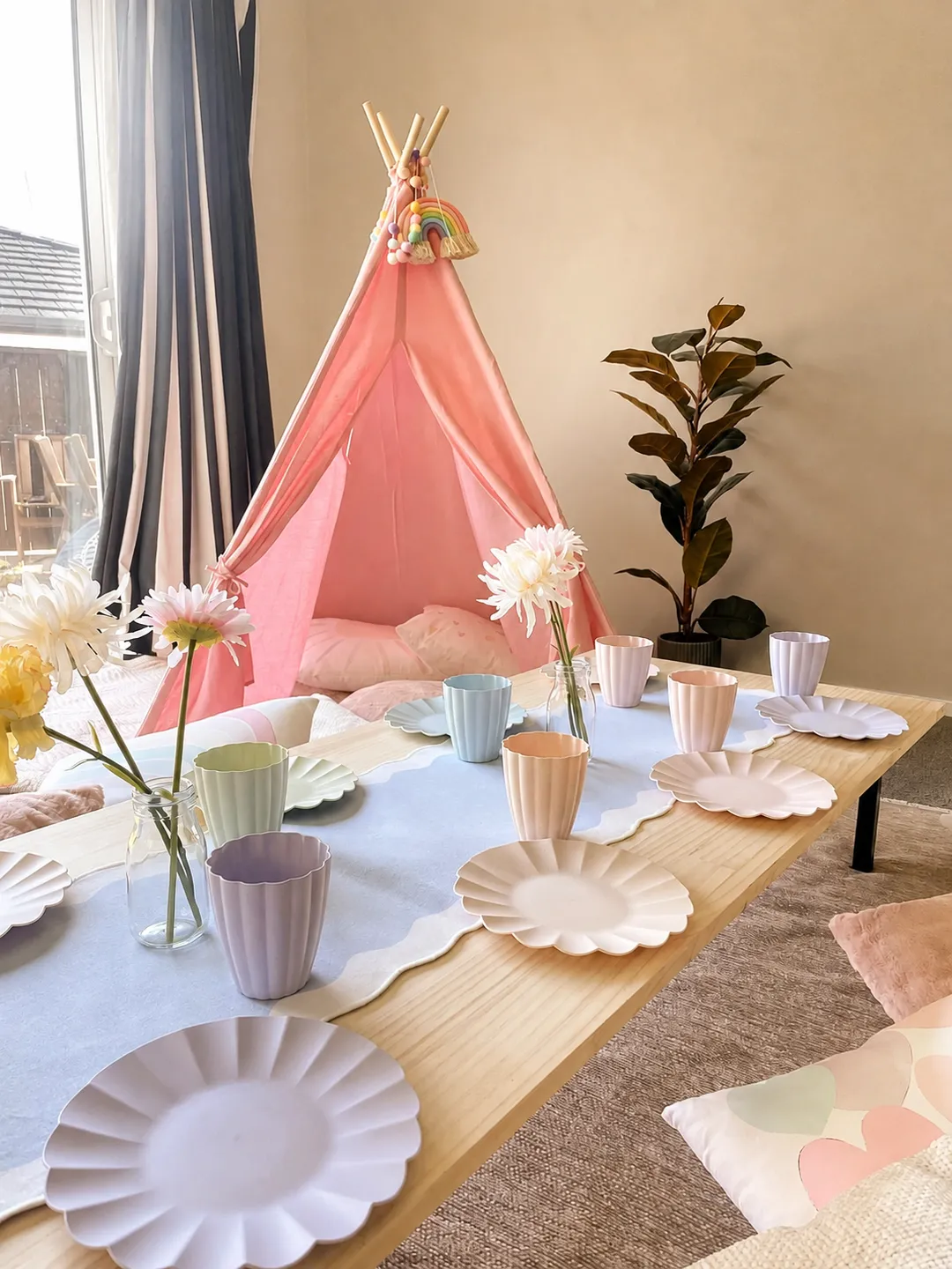 Pastel flower-shaped plates and cups arranged around the low picnic table beside the pink teepee.
